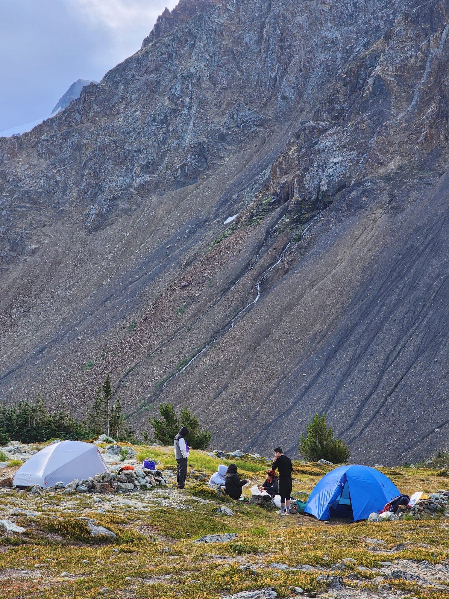 Friends gathered between tents beneath a massive scree slope