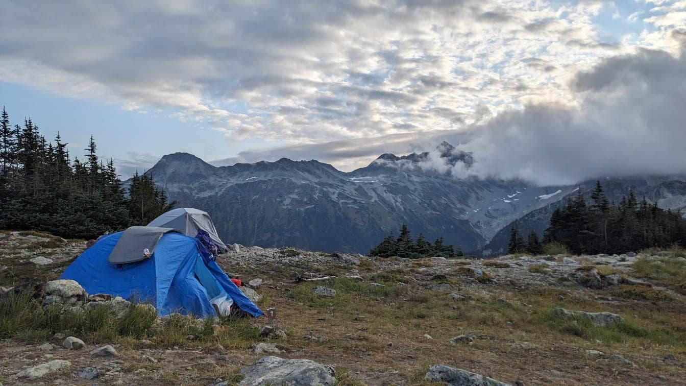 Blue tent pitched on rocky alpine ground with cloud-wrapped peaks behind