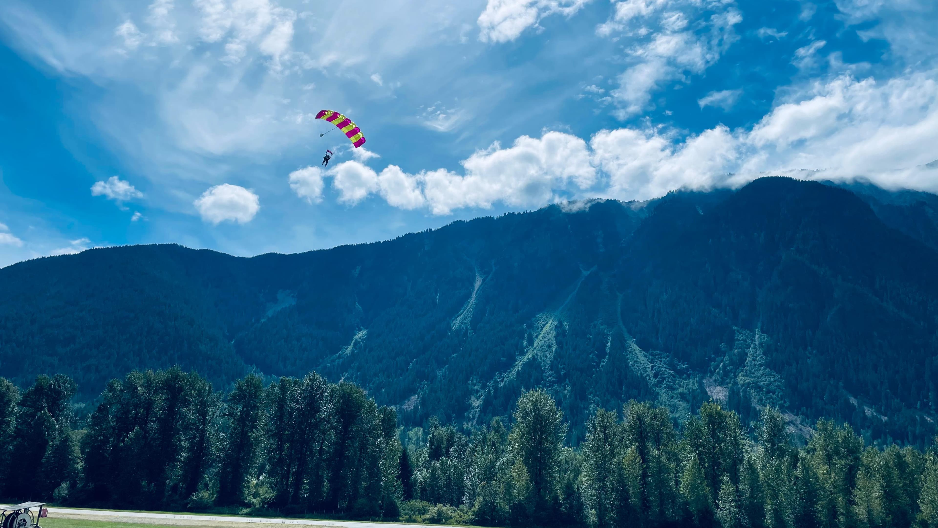A pink and yellow parachute high over a forested mountain ridge