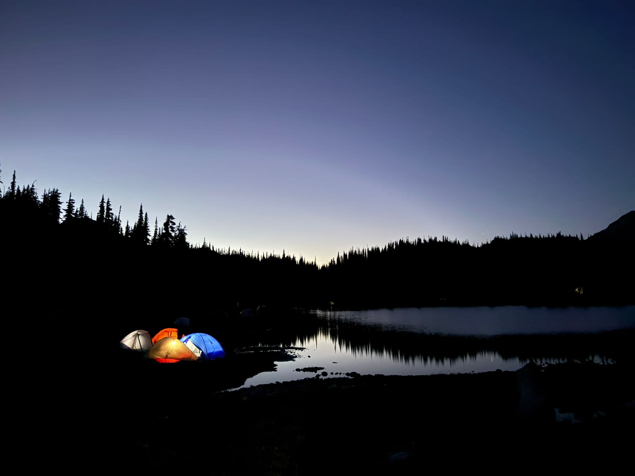 Glowing tents beside a still alpine lake at dusk in the BC backcountry